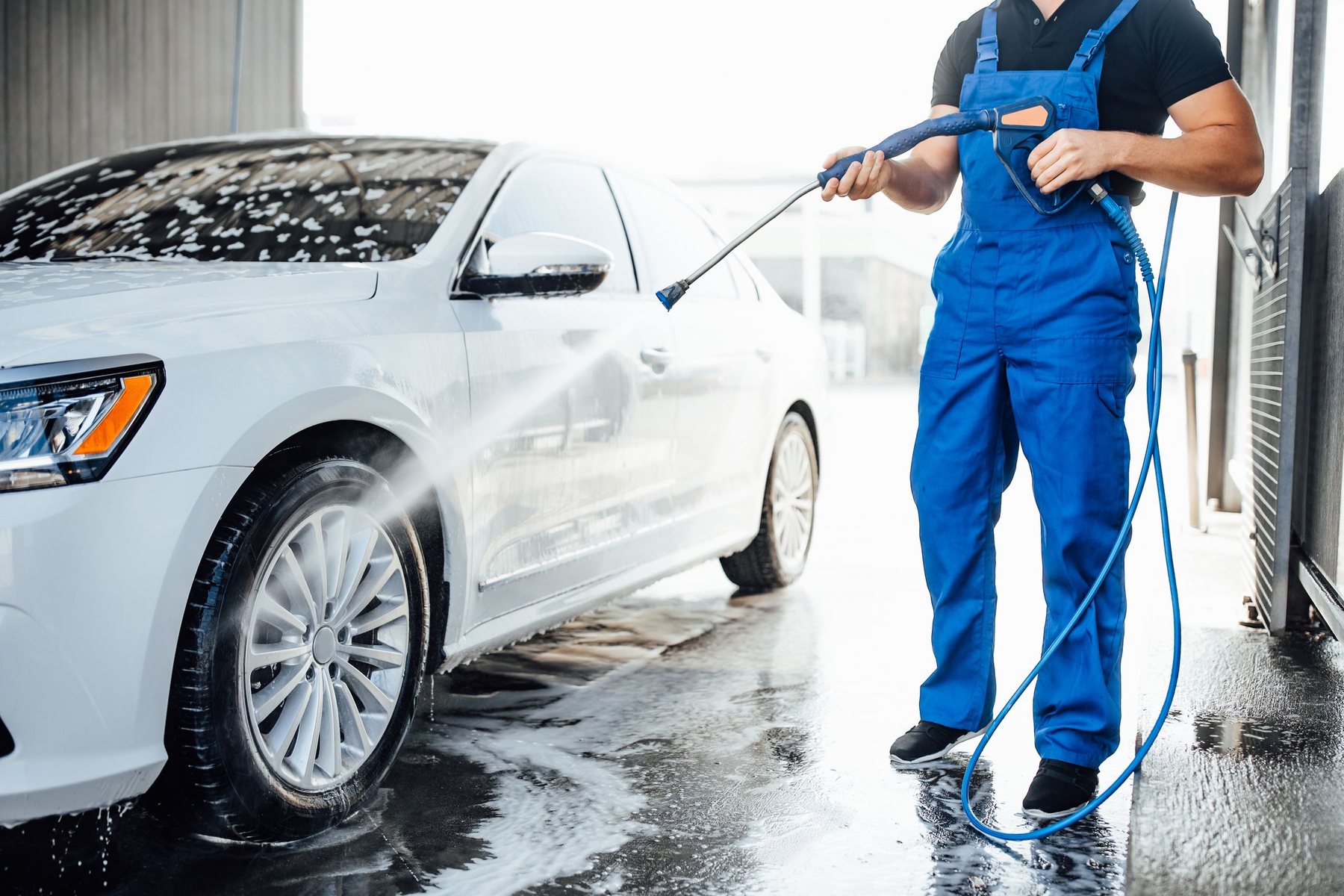 A professional cleaning a car with pressure wash foam